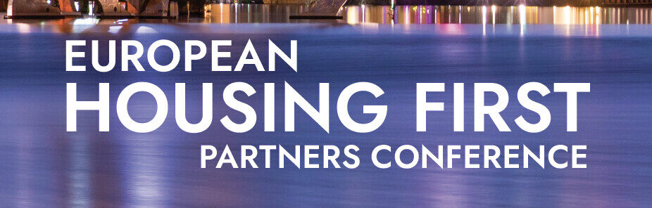 Der Text "European Housing First Partners Conference" erscheint in fetten weißen Buchstaben über einem Hintergrund, der eine städtische Uferpromenade mit verschwommenen Reflektionen bunter Lichter auf dem Wasser zeigt.